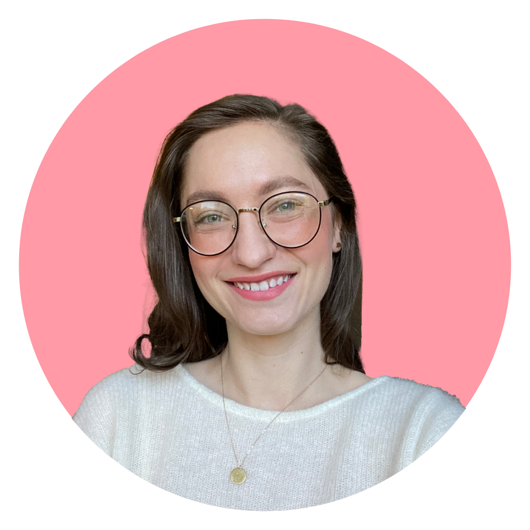 Alli is pictured from the shoulders up, smiling. She is white with green eyes and long brown hair. She wears a white sweater and round glasses.